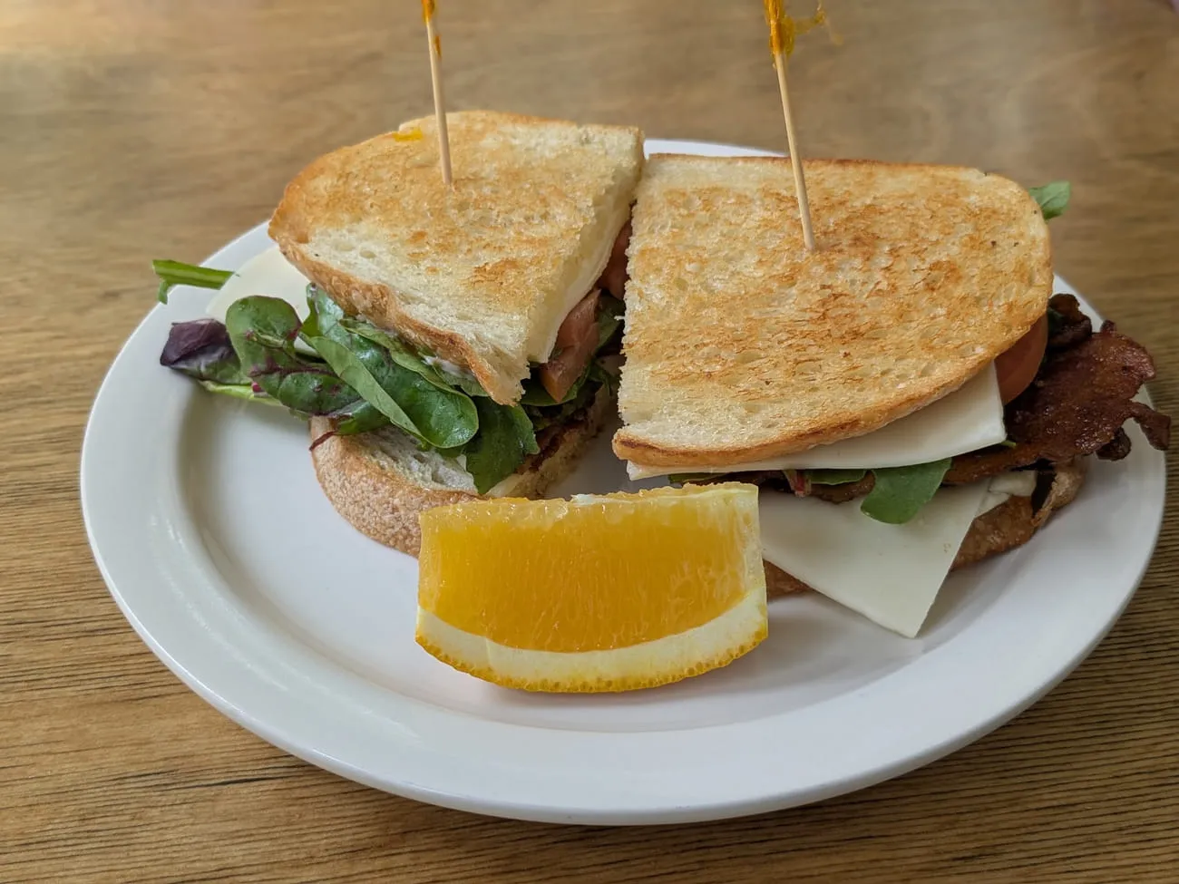 BLT sandwich on toasted bread cut in half, served with an orange wedge