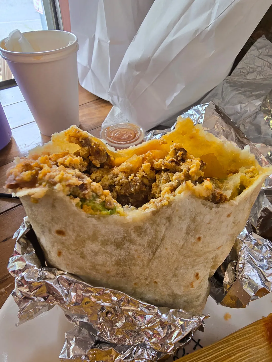Breakfast burrito opened up, filled with scrambled eggs, chorizo and potatoes, with a cup of salsa
