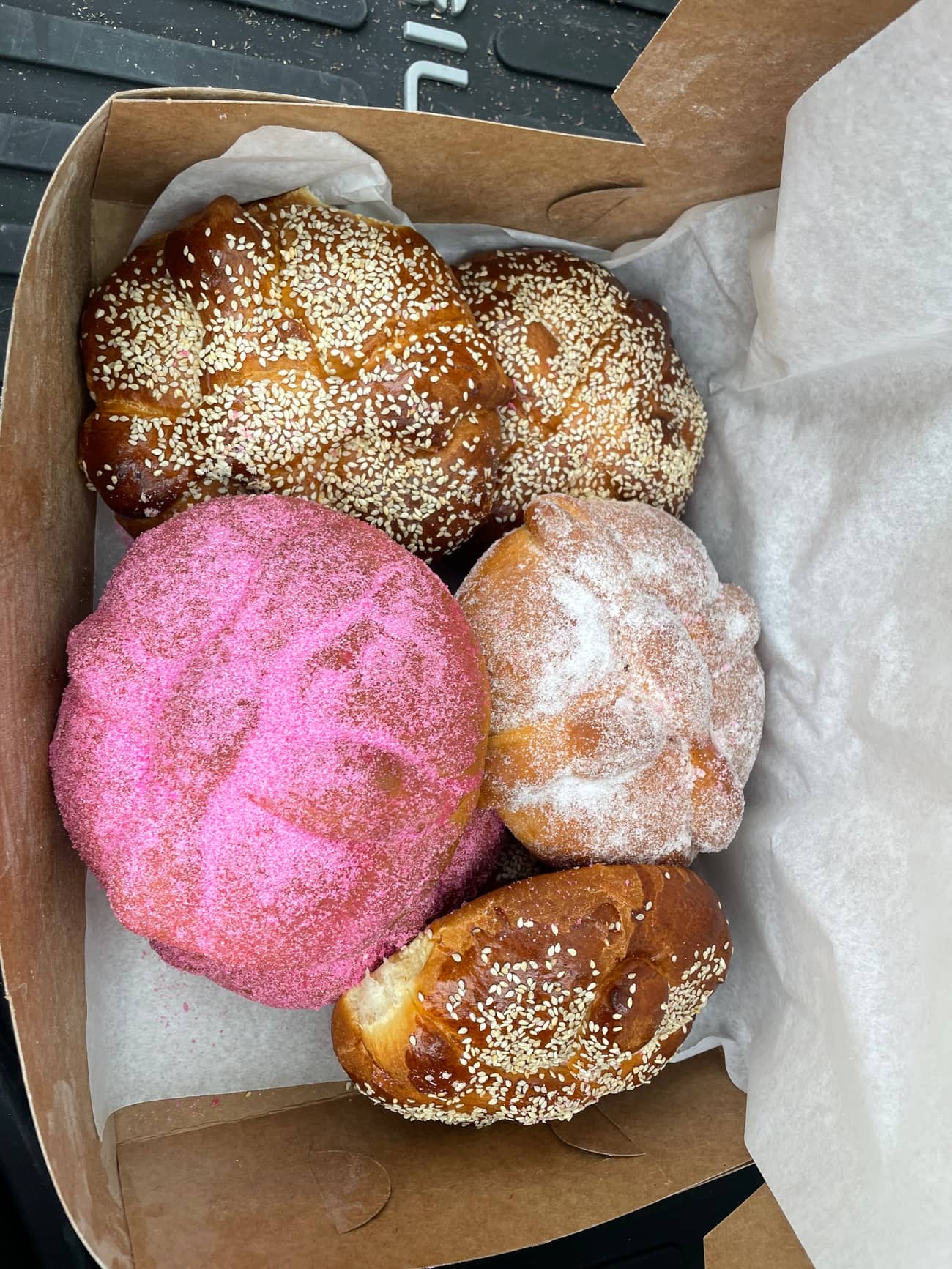 Box of pan dulce: a pink concha, a sugar-dusted concha and sesame-topped sweet breads