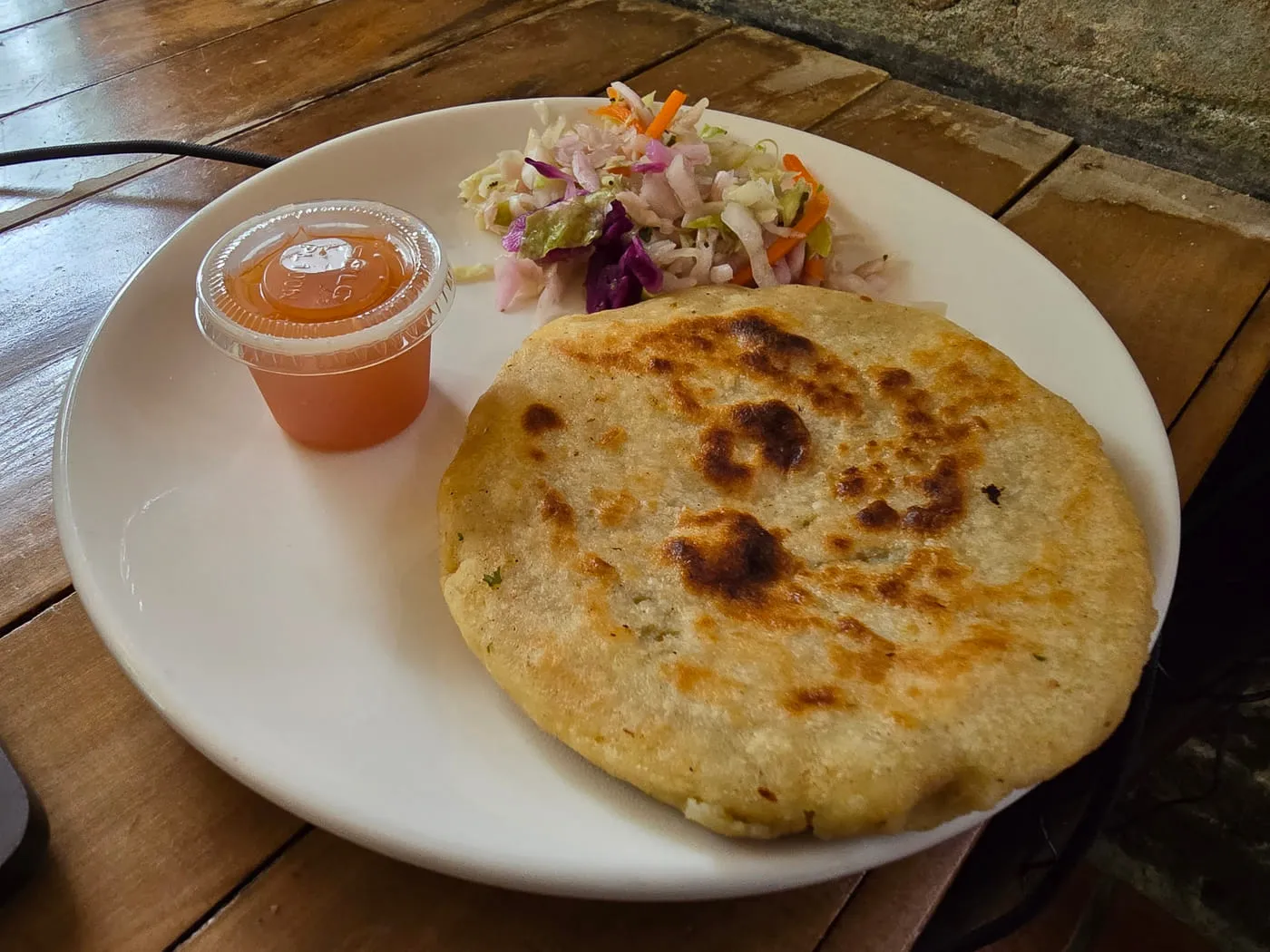 Pupusa served with curtido and salsa on a white plate