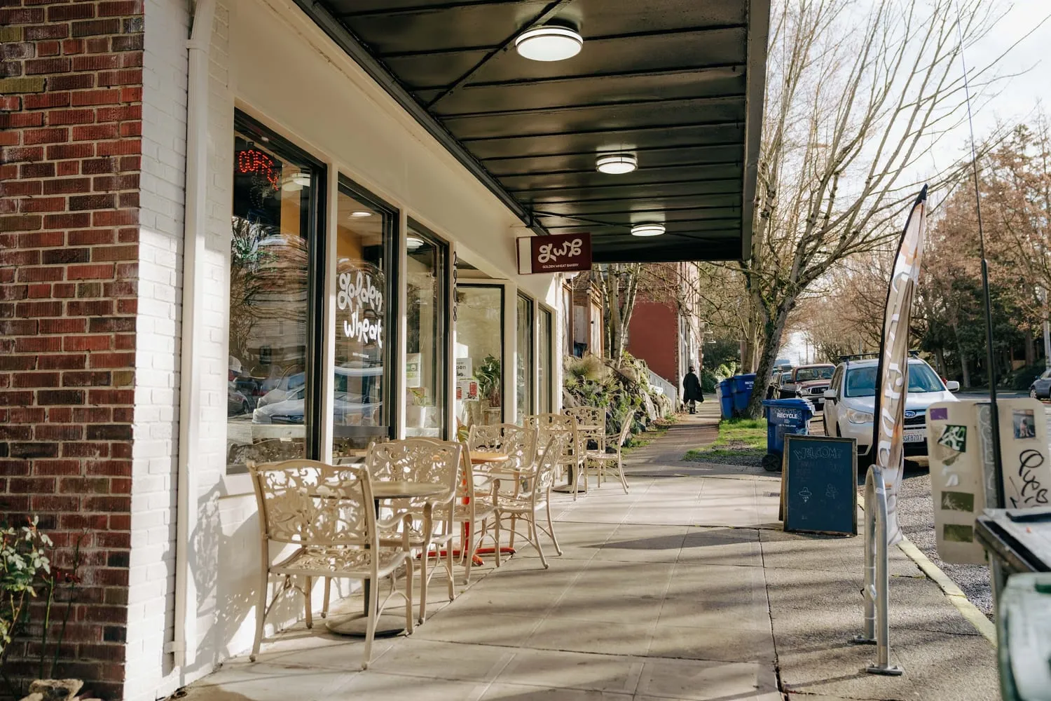 The sidewalk outside the bakery with café chairs, the hanging sign and the window lettering