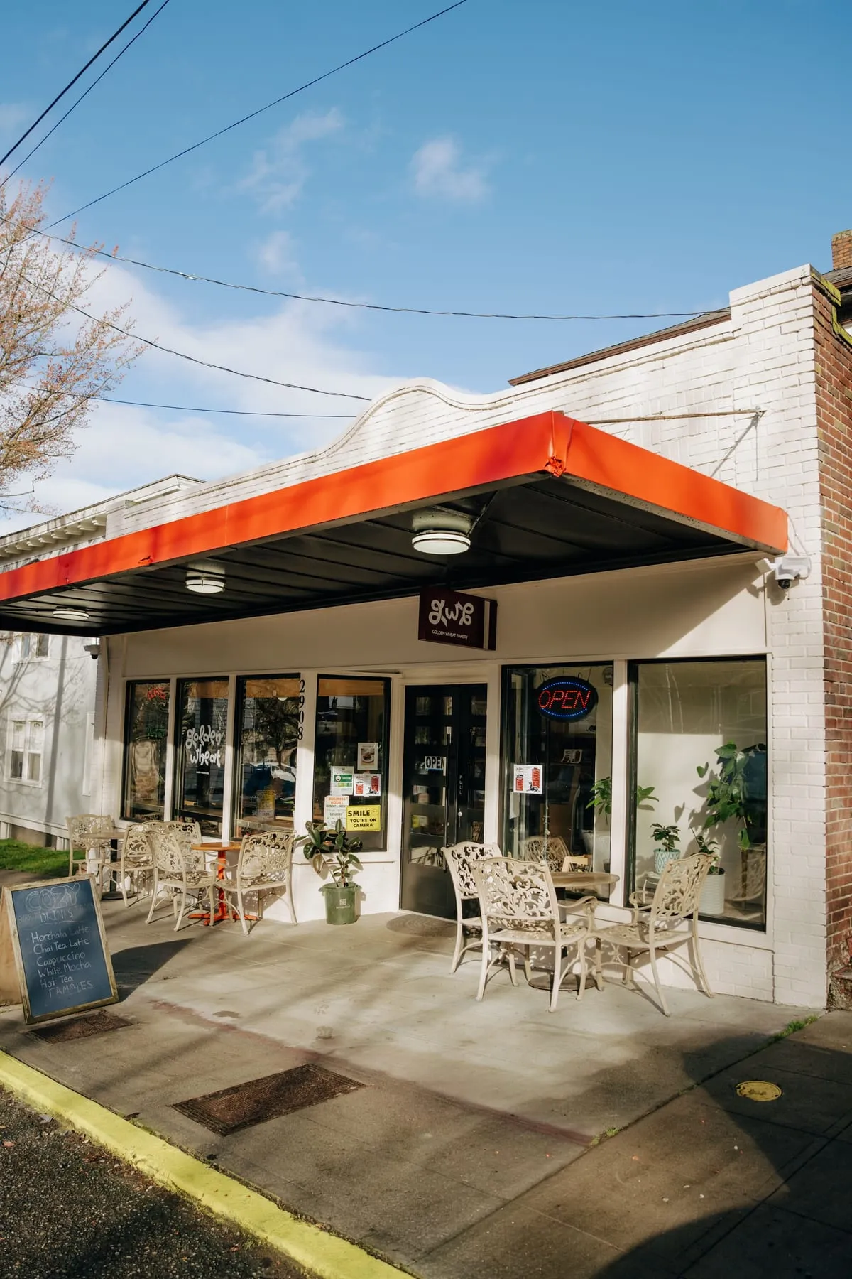 The corner storefront of Golden Wheat Bakery with its orange awning and sidewalk tables on E Cherry Street